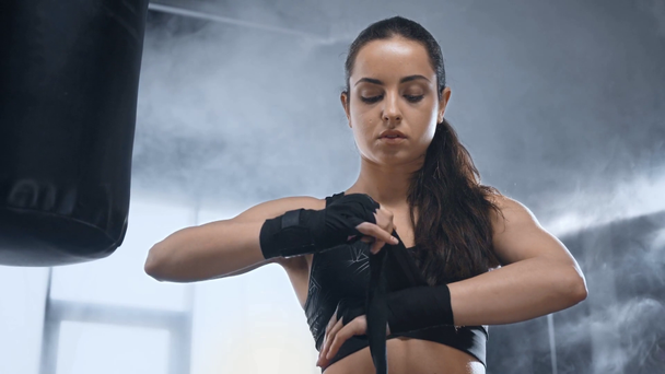 mooie Sportvrouw het verbinden handen in de buurt van ponsen tas in sportcentrum met rook - Video