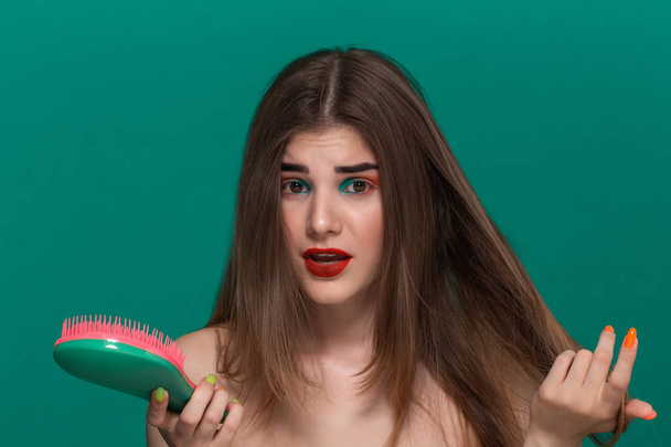 Portrait of beautiful young woman with bright color make-up combing hair with a green brush - Photo, Image