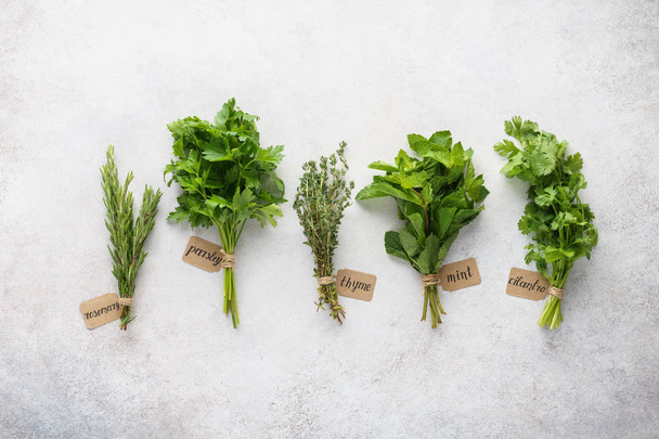 Various fresh herbs with paper tags on gray background. - Foto, afbeelding