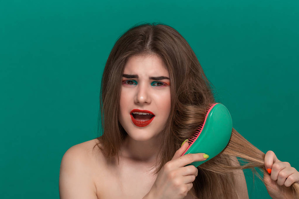 Portrait of beautiful young woman with bright color make-up combing hair with a green brush - Valokuva, kuva