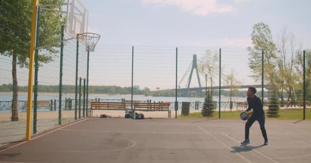 Portrait of sporty attractive african american male basketball player throwing ball into a hoop and failing being frustrated on court in the urban city outdoors with bridge on the background - Materiaali, video