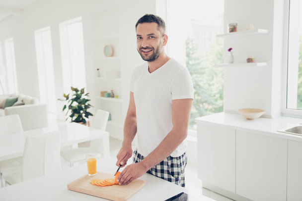 Close up side profile photo attractive he him his homey guy cheerful positive vacation hobby preparation favorite fruit salad meal dish white t-shirt checkered pants bright kitchen room indoors - 写真・画像