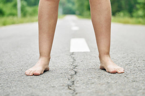 アスファルト道路に立つ若い女の子の裸足がクローズアップ. - 写真・画像