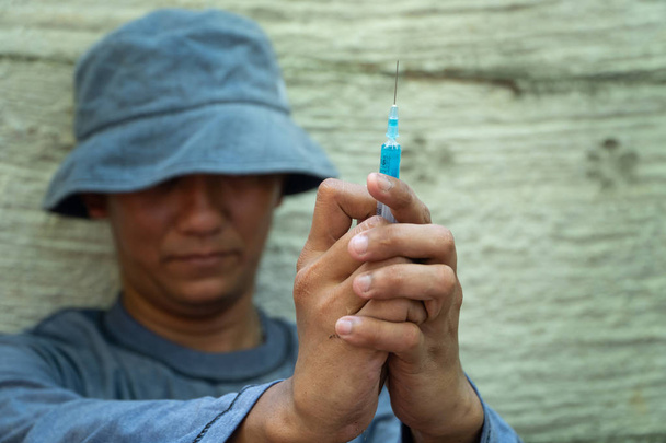 close up of Syringe and Needle in hand of drug addict man. homeless using needle injecting liquid. Drug concept and Danger of drugs - Photo, image