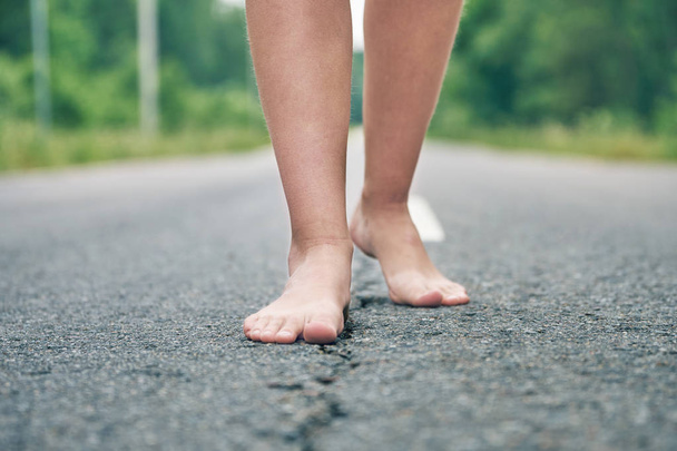 Γυμνά πόδια ενός νεαρού κοριτσιού που περπατά κατά μήκος του ασφαλτοστρωμένου δρόμου - Φωτογραφία, εικόνα