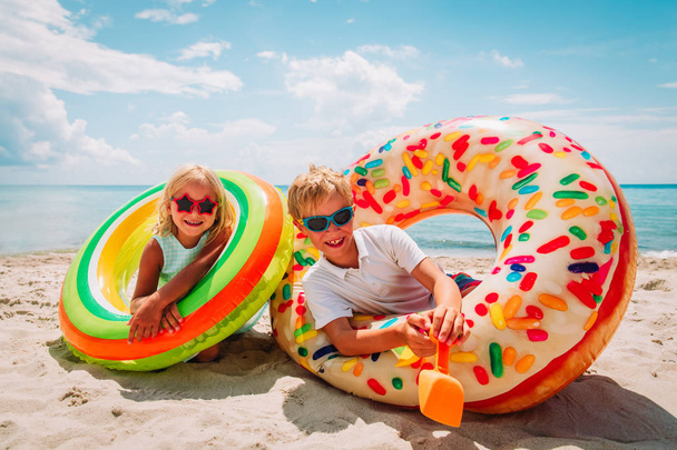 happy cute boy and girl play with floaties on beach - Foto, afbeelding