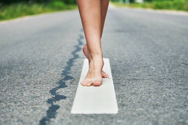 Τα γυμνά πόδια ενός νεαρού κοριτσιού στέκονται στη γραμμή του διαιρεστού δρόμου - Φωτογραφία, εικόνα
