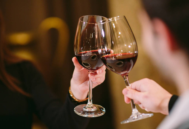 Άντρας και γυναίκα πίνουν κόκκινο κρασί. Στην εικόνα, κοντά χέρια με γυαλιά. - Φωτογραφία, εικόνα
