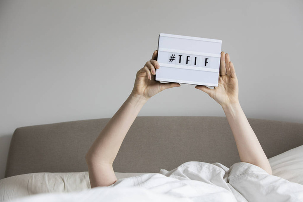 Female in bed under the sheets holding up a TFIF sign - Photo, image