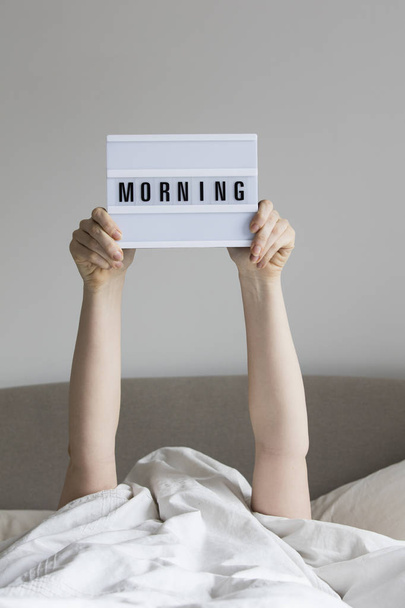 Female in bed under the sheets holding up a morning sign - Fotó, kép