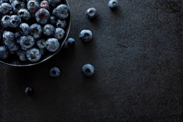 Fresh blueberries in a dark ceramic bowl on a black background, top view, close-up. Organic fruits - Photo, image