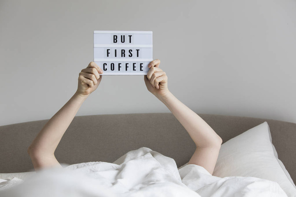 Female in bed under the sheets holding up a but first coffee sig - Foto, afbeelding
