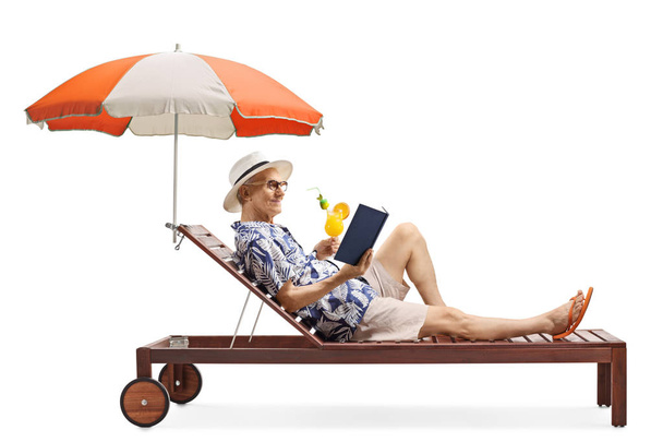 Homem sênior desfrutando em uma espreguiçadeira com um livro e um coquetel
 - Foto, Imagem