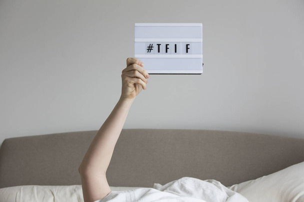 Female in bed under the sheets holding up a TFIF sign - Foto, afbeelding