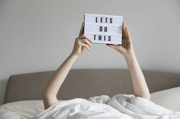 Female in bed under the sheets holding up a lets do this sign - Photo, Image
