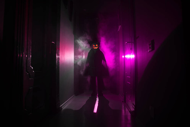 Halloween concept. Griezelig silhouet in de donkere gang met pompoen hoofd. Licht getint met mist op de achtergrond. Selectieve focus - Foto, afbeelding