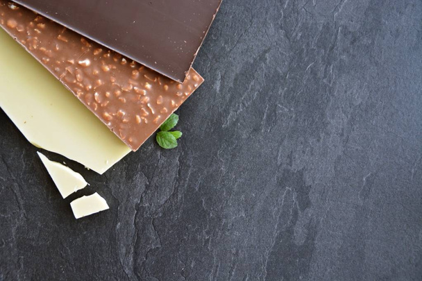 Trois barres de chocolat noir, noix et chocolats blancs reposent sur une surface de marbre noir chocolat sur une surface sombre avec de la place pour le texte ou d'autres éléments
 - Photo, image