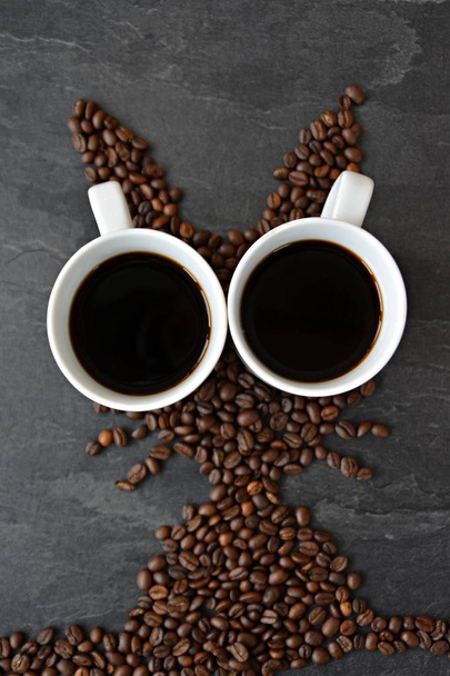 An Easter bunny made of freshly roasted coffee beans laid out with a cup of coffee - concept for fresh coffee enjoyment on easter and as easter gift in the form of coffee beans - Photo, Image