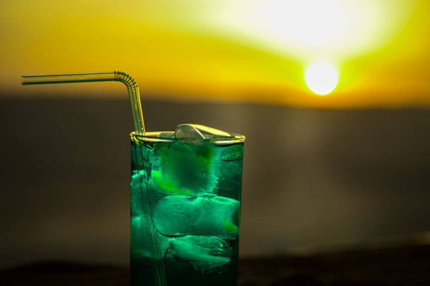 Close-up nat glas van groene koude Mint drankje, kleurrijke oranje zonsondergang achtergrond op het terras. Koeling zomer drankje. Zomer fris en koel inspiratie, avond contrast kleurencombinatie. - Foto, afbeelding