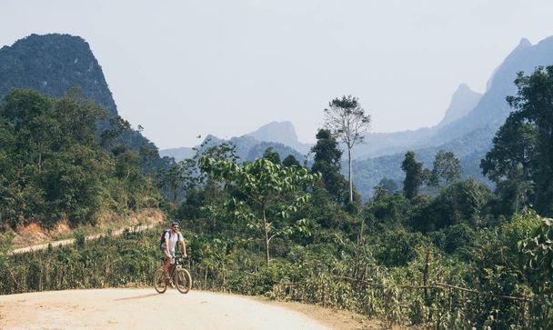 Mladý Kavkazský muž jedoucí na horském kole do kopce v Muang Nindické vesnici, Laos - Fotografie, Obrázek