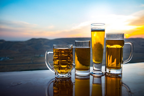 Um copo de cerveja numa praia ao pôr-do-sol. Conceito de bebida refrescante de verão. Close Up of A Glass of Draught Beer with the Bokeh of Sunlight Background
 - Foto, Imagem