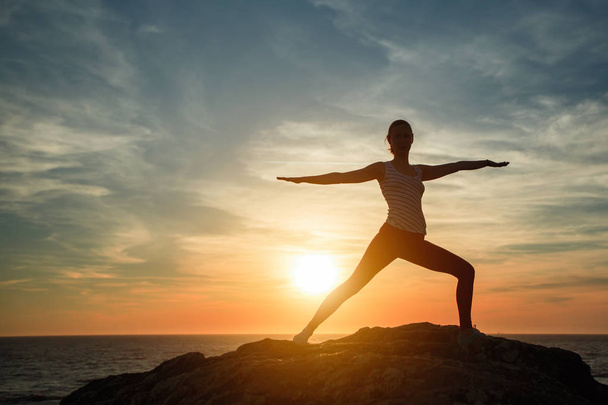 Silhouette einer Yoga-Frau bei Fitnessübungen am Strand des Ozeans bei Sonnenuntergang. - Foto, Bild