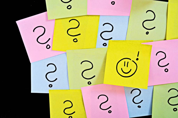 On a dark background stuck differently colored pieces of paper, many have a question mark painted on it, one has drawn a smilie on it. Concept for brainstorming and creative work - Photo, Image