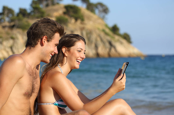 Casal feliz na praia verificando tablet
 - Foto, Imagem
