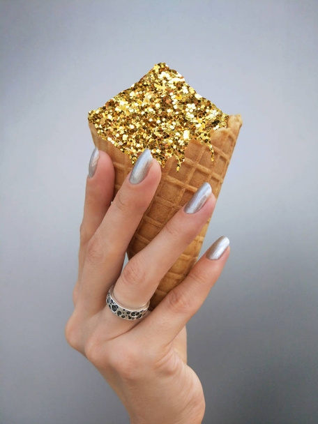 hand holding golden ice cream on silver background.Golden tinsel sparkles creative pop art - Fotó, kép