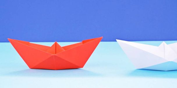 Un bateau en papier autoplié rouge repose sur une surface bleue, suivi de nombreux bateaux blancs concept symbolisant le leadership
 - Photo, image