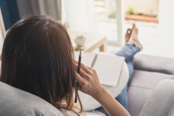Young woman writing diary at cozy home on sofa in living room - Photo, image