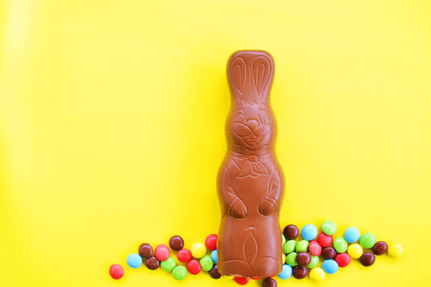 Ein Osterhase aus Schokolade mit bunten Schokoladenstücken auf der Außenseite liegt auf einer Einzweck-Oberfläche - Süßigkeiten Ostern auf einer farbigen Oberfläche - Foto, Bild