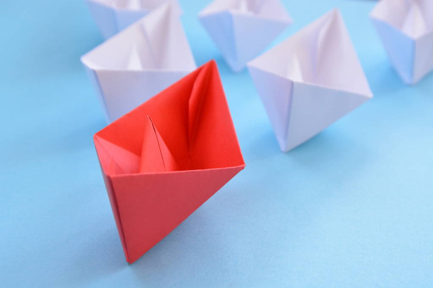 赤い自己折りたたみ紙ボートが青い表面に横たまり、その後に多くの白いボートが続く - リーダーシップを象徴するコンセプト - 写真・画像
