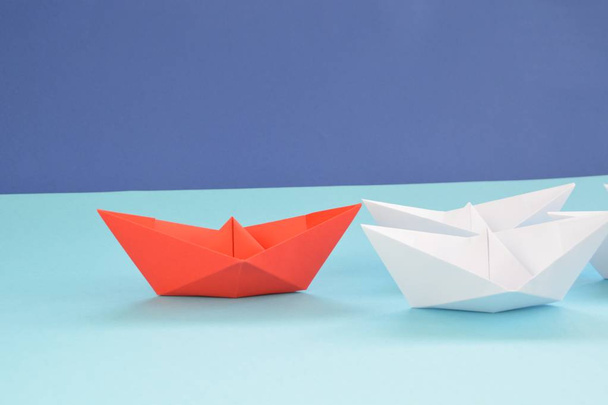 A red self-folded paper boat lies on a blue surface, followed by many white boats - concept symbolizing leadership - Фото, изображение