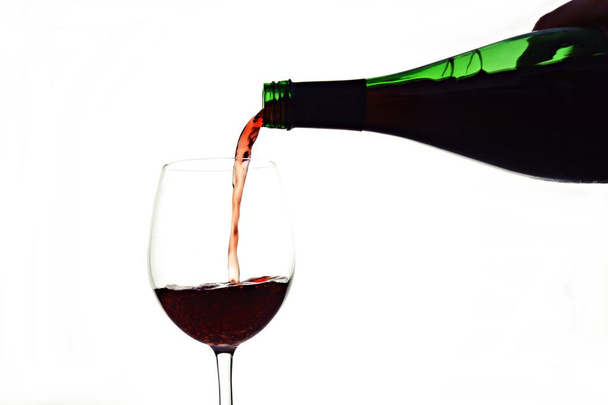 白い背景に対してボトルからガラスにワインを注ぐクローズアップビュー - 写真・画像