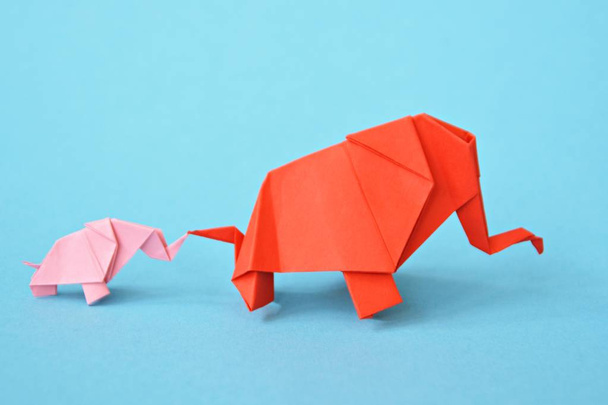 ピンクと赤の2頭の紙折り象が青い背景に立つ - 小さな赤ちゃんゾウと折り紙の技術に従って折り畳まれた母ゾウとのコンセプト - 写真・画像