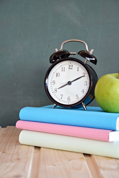 Az ébresztőóra előtt áll egy tábla színes könyvek és egy zöld alma-koncepció helyet szöveget vagy egyéb elemeket a témában az iskola és az időgazdálkodás az elemi iskolában - Fotó, kép