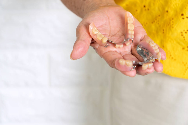 Mulher idosa asiática com mais de 70 anos segurando dentaduras na mão. Dentaduras para dispositivos protéticos construídos para substituir dentes perdidos e ajudar a mastigar alimentos. A capacidade de mastigar alimentos de idosos
 - Foto, Imagem
