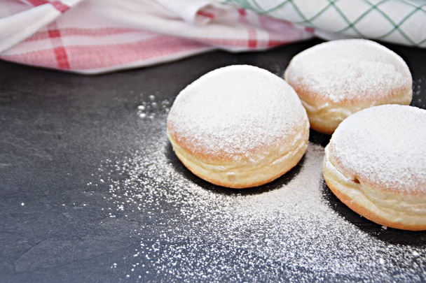 The so-called Krapfen, which are traditionally baked in Germany during the carnival season, lie on a dark surface - donuts sprinkled with powdered sugar - Photo, Image