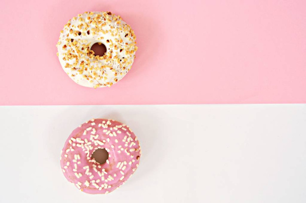 Two donuts, one pink with crumble and one white with brittle lie on a half pink, half white area - The donuts each have the opposite color to the ground. Concept with donuts and colors as a background - Foto, Imagen