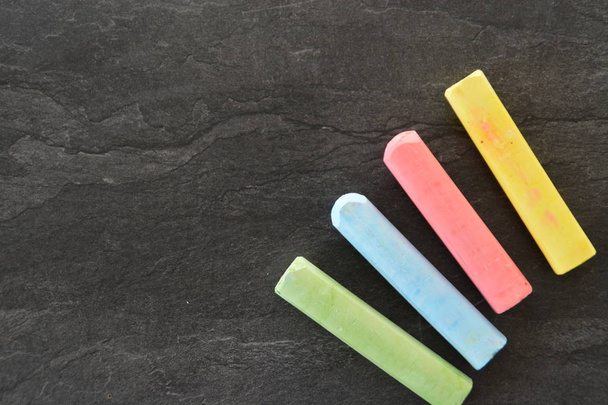 Different colored chalks lie on a dark marble surface - concept as a background with colorful chalks and place for text or other elements  - Photo, Image