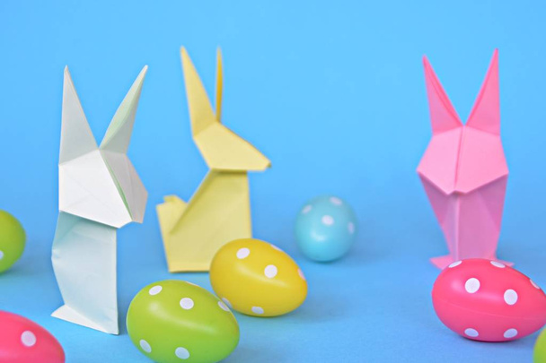 Origami bunnies folded from pastel paper stand on a blue base with dotted easter eggs on the outside - concept with origami for Easter with strong colors - Photo, Image