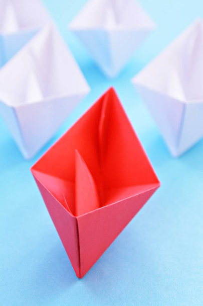 赤い自己折りたたみ紙ボートが青い表面に横たまり、その後に多くの白いボートが続く - リーダーシップを象徴するコンセプト - 写真・画像