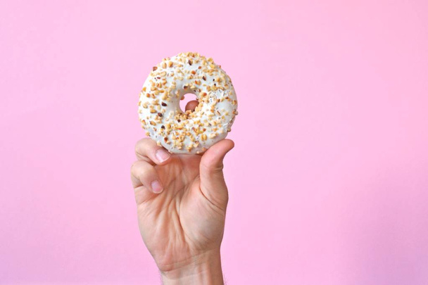 A hand holds a donut with chocolate icing upwards. The background is colored and leaves room for text or other elements - Foto, Imagen