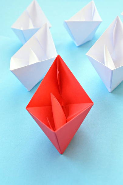 Una barca di carta rossa auto piegata si trova su una superficie blu, seguita da molte barche bianche - concetto che simboleggia la leadership
 - Foto, immagini