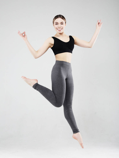 Sport, fitness and people concept: Beautiful young woman dressed in sportswear jumping up over grey background - 写真・画像