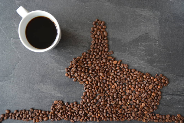 ein Osterhase aus frisch gerösteten Kaffeebohnen ausgelegt mit einer Tasse Kaffee - Konzept für frischen Kaffeegenuss zu Ostern und als Ostergeschenk in Form von Kaffeebohnen  - Foto, Bild