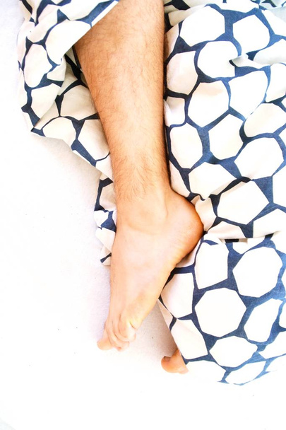 κοντινό πλάνο των ποδιών που προεξέχουν από το κρεβάτι - Φωτογραφία, εικόνα