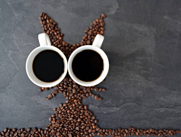ein Osterhase aus frisch gerösteten Kaffeebohnen ausgelegt mit einer Tasse Kaffee - Konzept für frischen Kaffeegenuss zu Ostern und als Ostergeschenk in Form von Kaffeebohnen - Foto, Bild