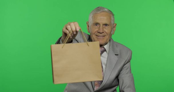 älterer Mann mit Einkaufstasche. blickt in die Kamera und streckt das Geschenk - Foto, Bild